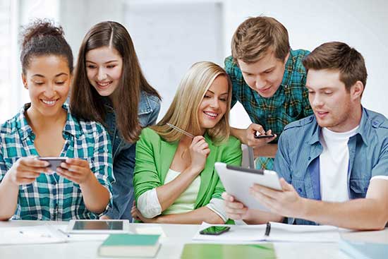 Group of high school students working with various digital devices.